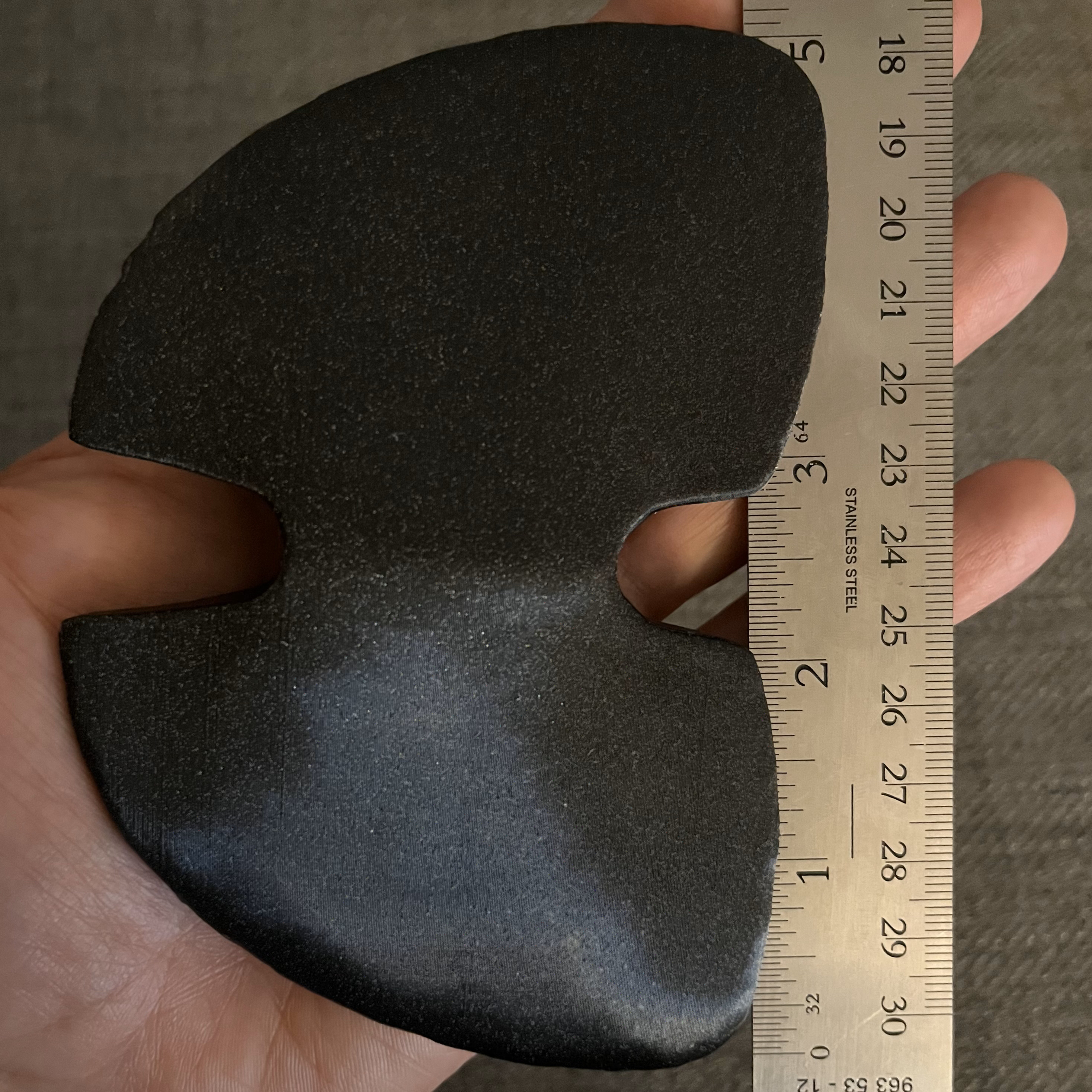 Hand holding the black Prusament winged bannerstone replica vertically alongside a standard ruler.